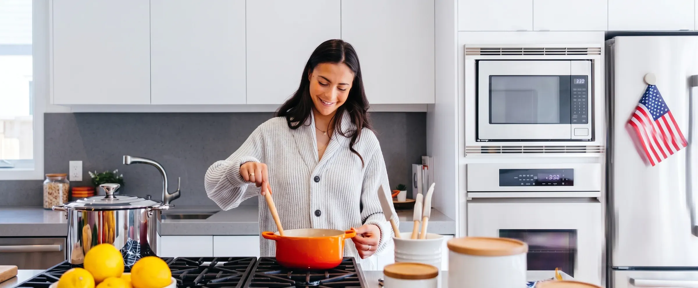Homeowner cooking at a range in a bright kitchen with a built-in microwave and white cabinets