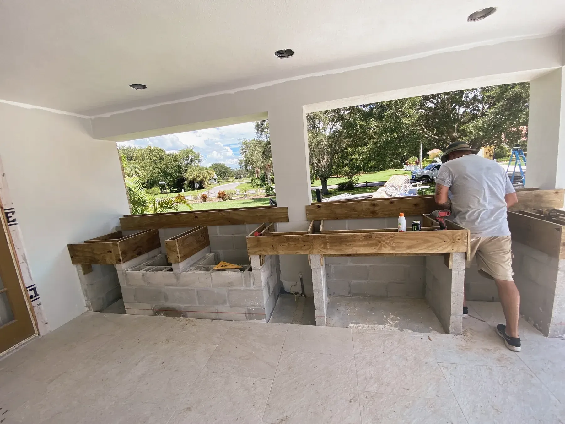 Worker, seen from behind, at the block and lumber frame of an outdoor kitchen on a covered patio