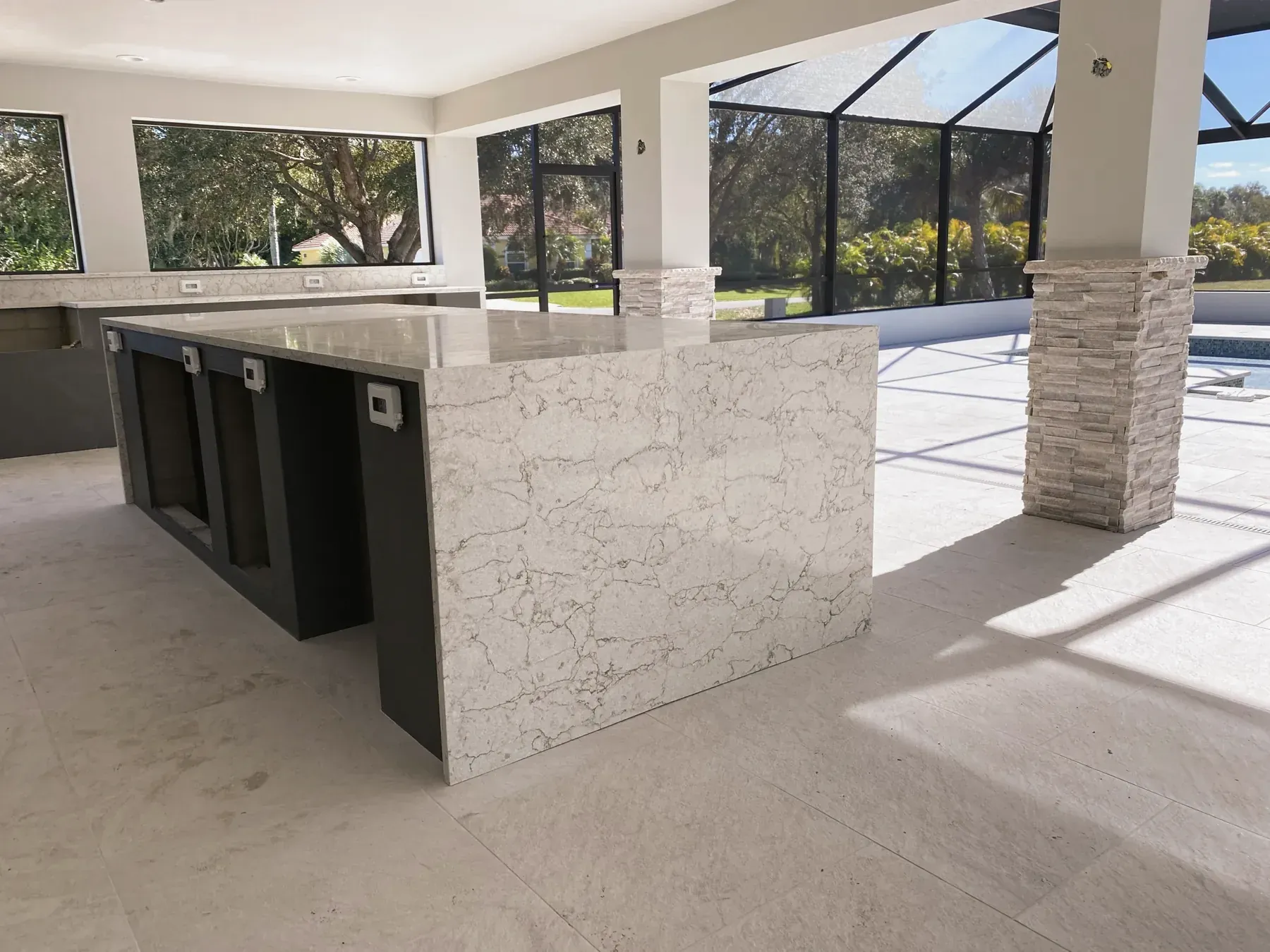 Close-up of a veined stone waterfall edge on dark base cabinets with a screened porch behind