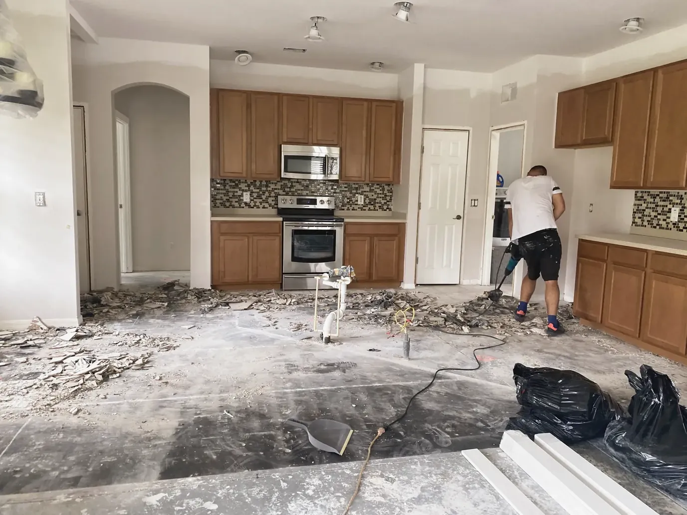 Kitchen demolition with wood cabinets and a worker removing flooring