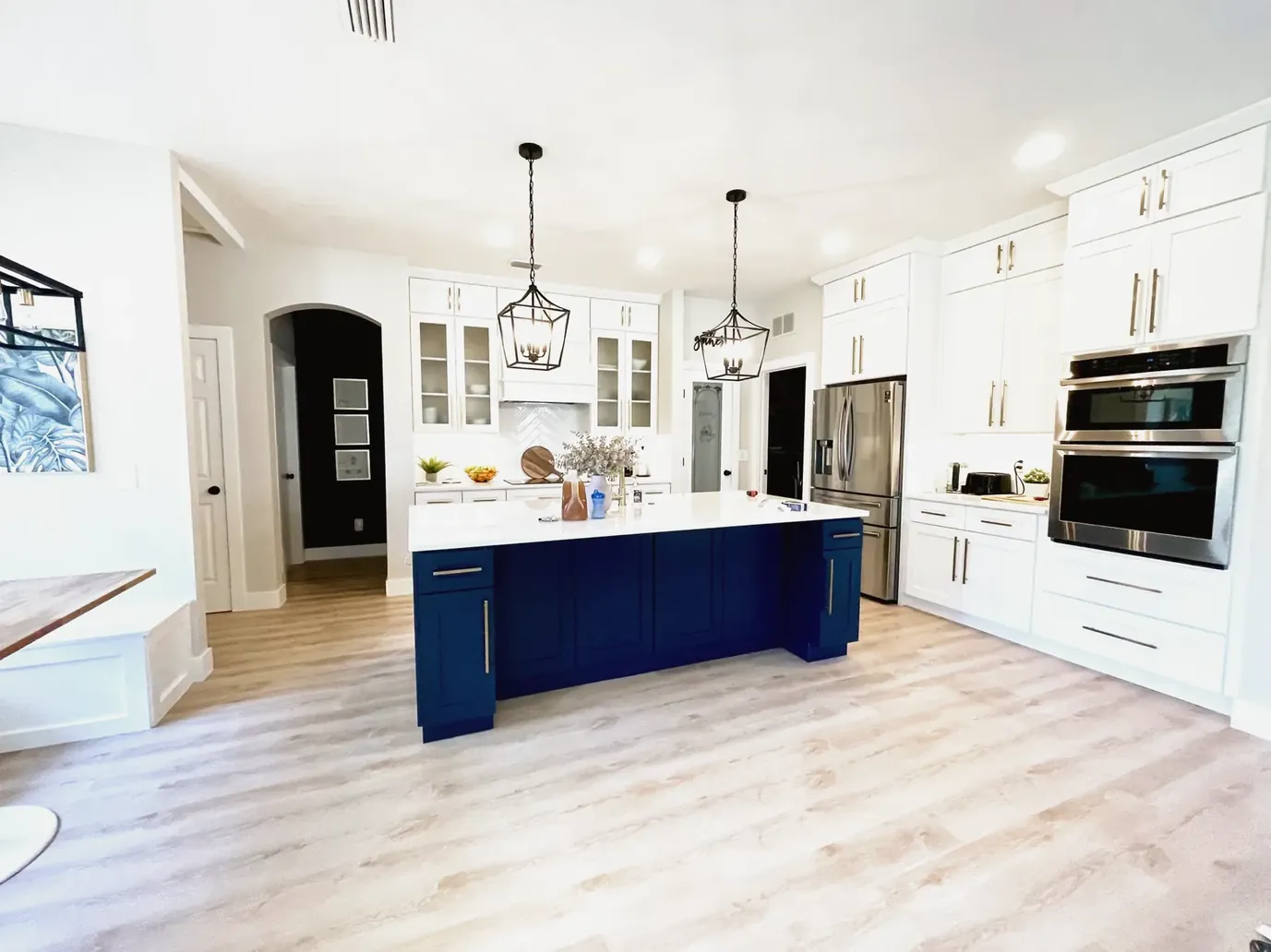 White shaker kitchen with a navy blue island, black lantern pendants and a built-in double oven