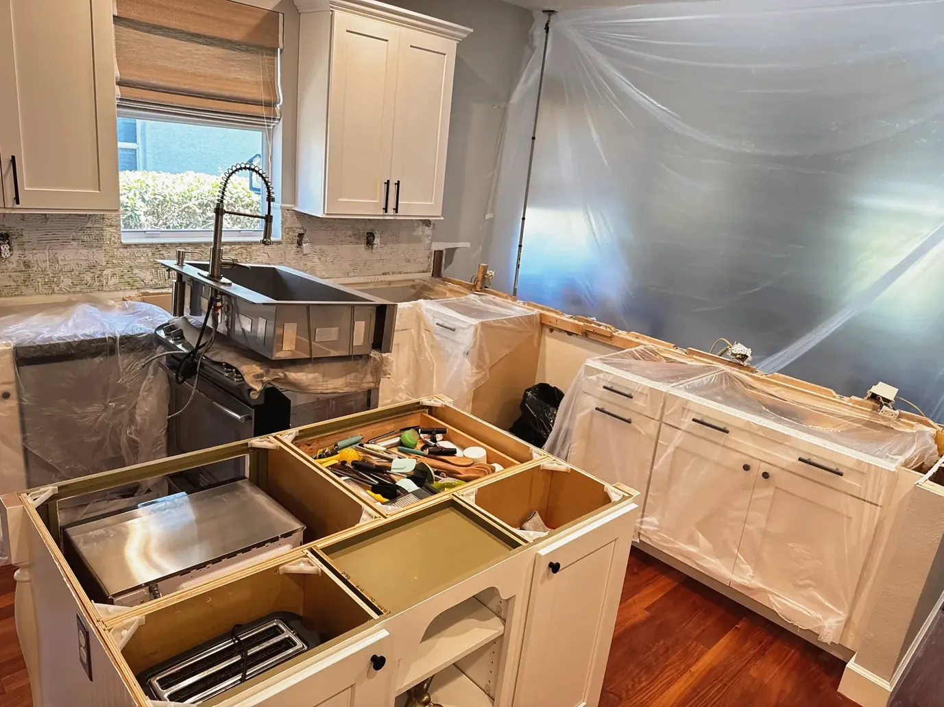 Kitchen under construction behind plastic dust sheeting, with base cabinet boxes set in place and tools resting on top