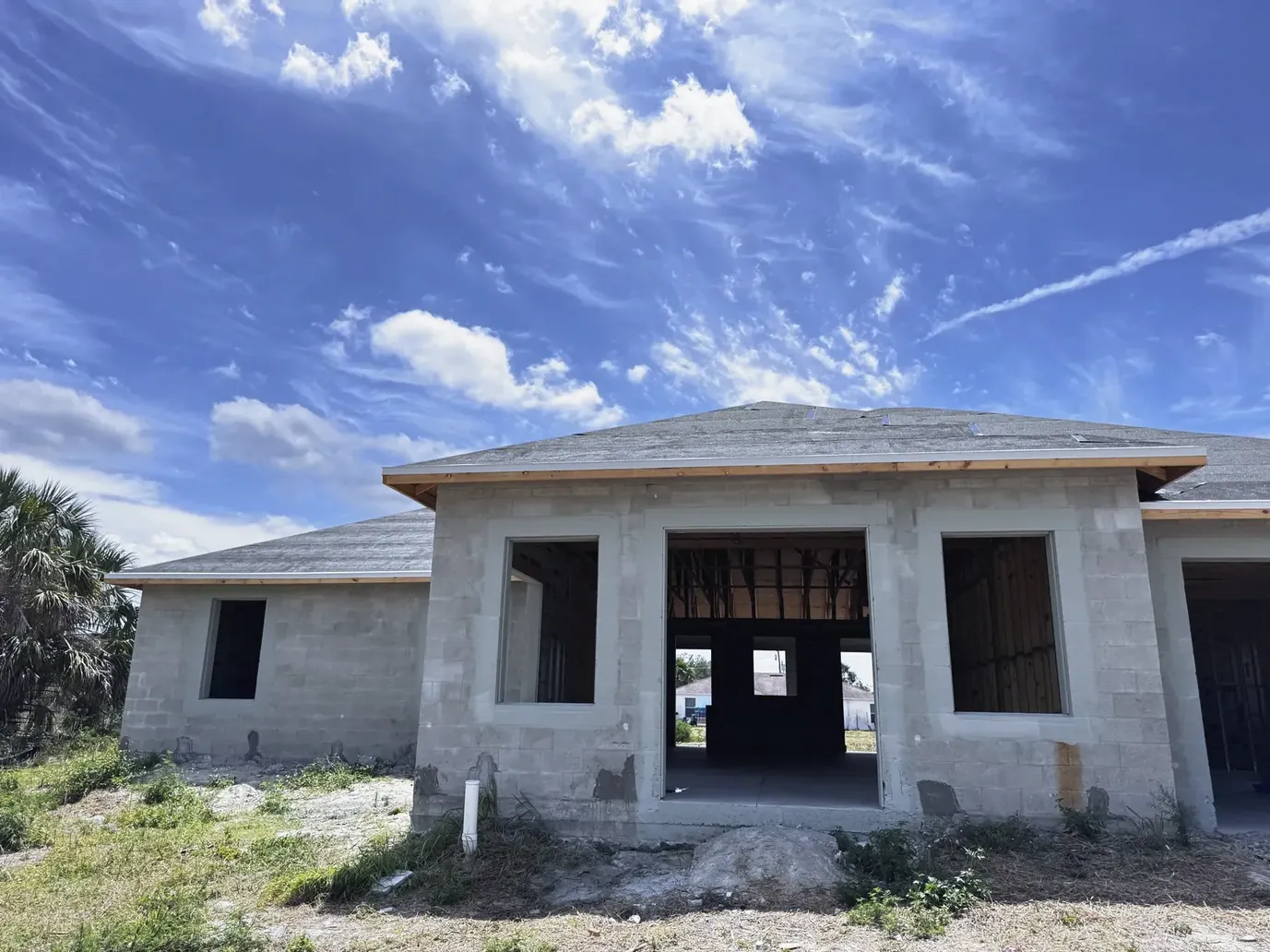 Concrete-block house shell with open window and door openings under a large cloudy blue sky