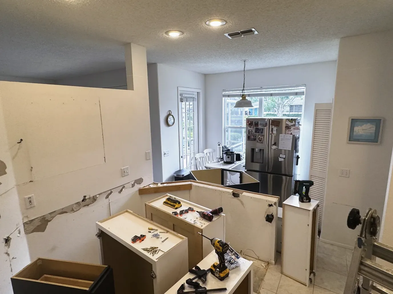 Cabinet bases with tools on top in a kitchen opened down to the wall surfaces, with a window and trees beyond