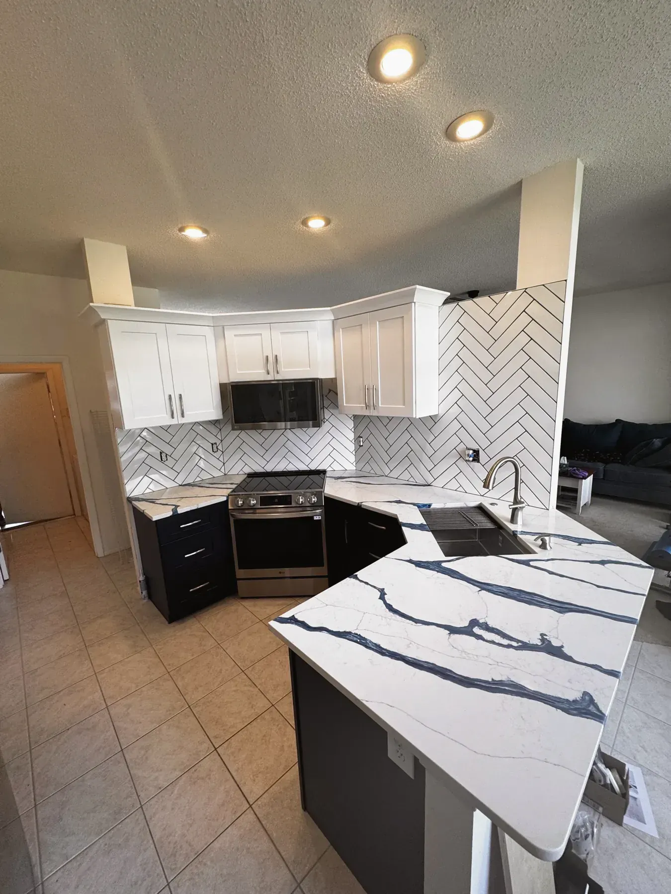 Kitchen corner with navy lower cabinets, a herringbone tile backsplash and a white countertop with dark gray veining