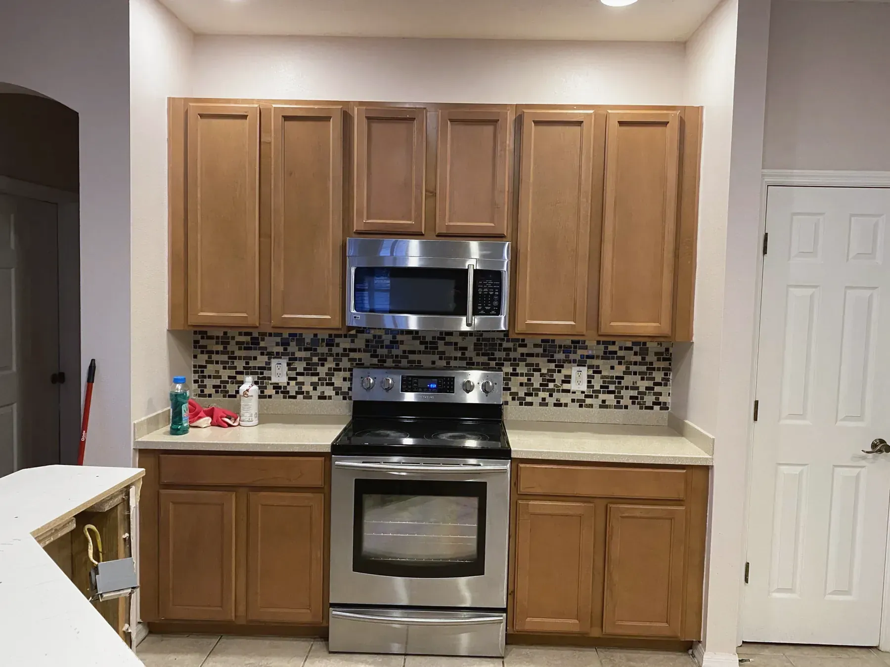 Kitchen with honey-oak cabinets, a dark mosaic tile backsplash and a stainless steel range, before renovation