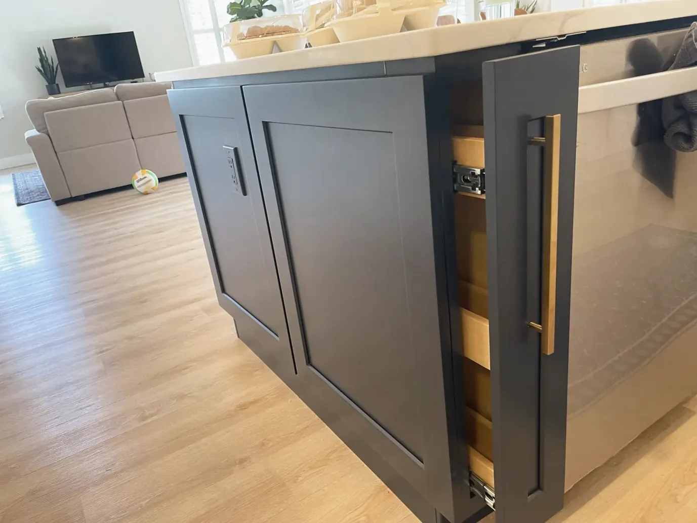 Navy blue shaker cabinet end with a narrow pull-out unit partly open and a brass bar pull