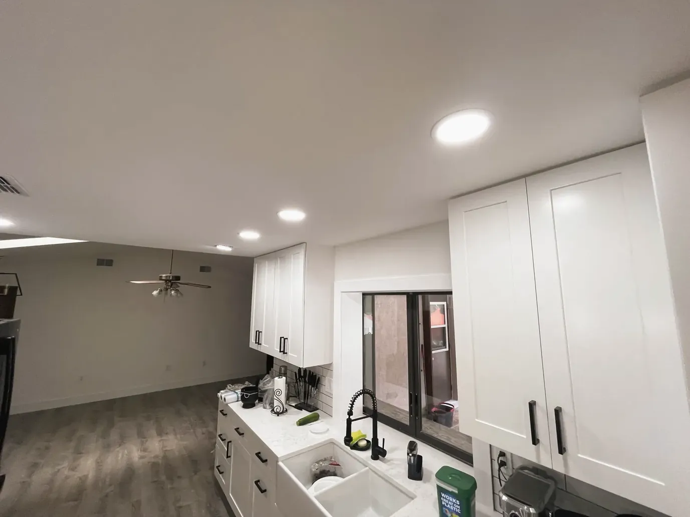 White shaker cabinets and a white sink with a black faucet along one wall of a mostly empty room