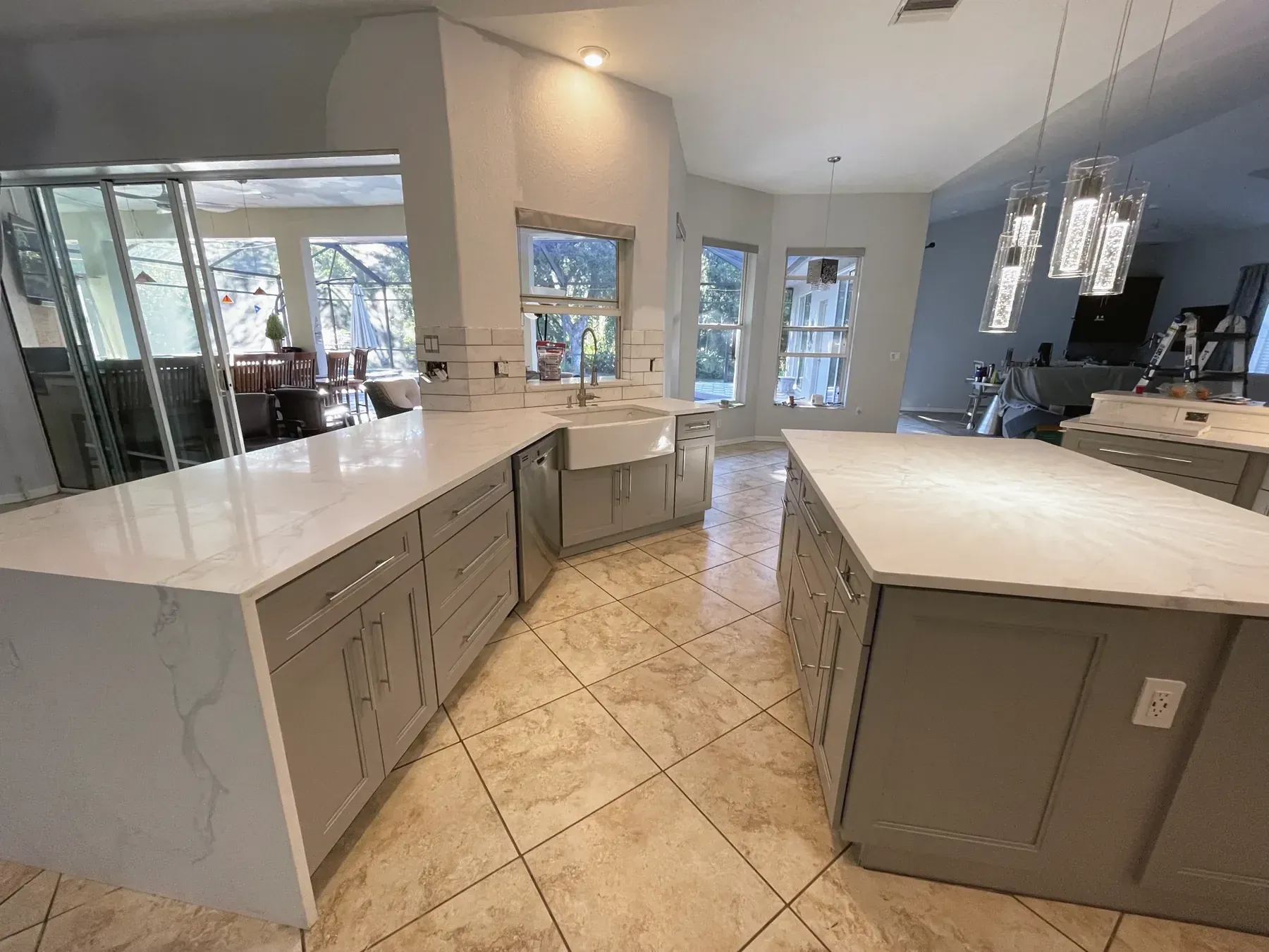 Gray shaker kitchen with two white waterfall-edge islands and a farmhouse sink below a row of windows