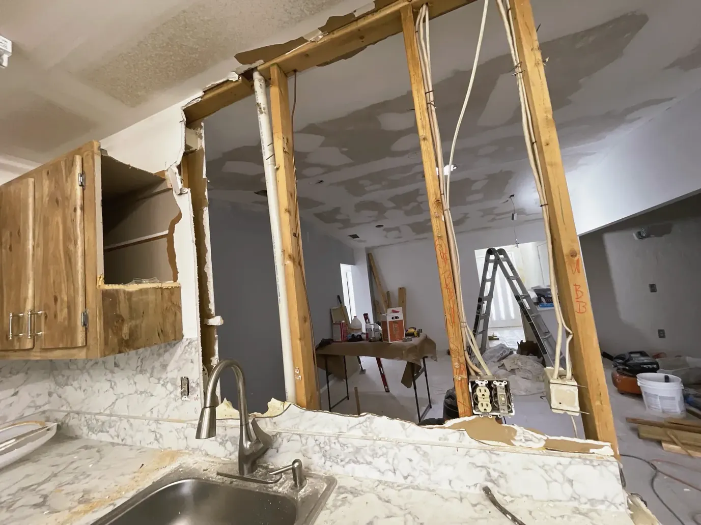 Kitchen wall opened down to the studs, next to old cabinets and a stainless steel sink