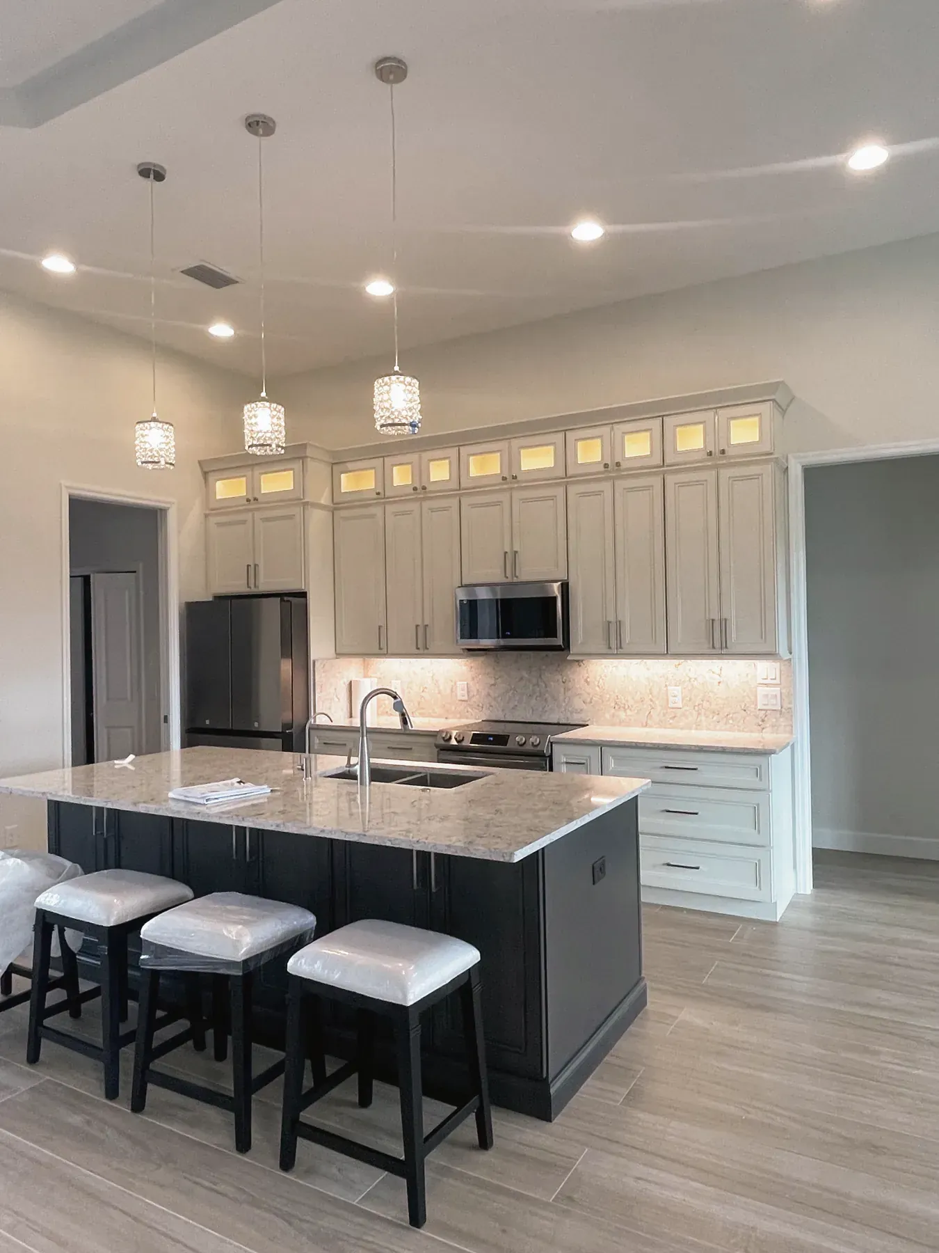Kitchen with lit upper cabinets, a dark island with three bar stools and a high ceiling