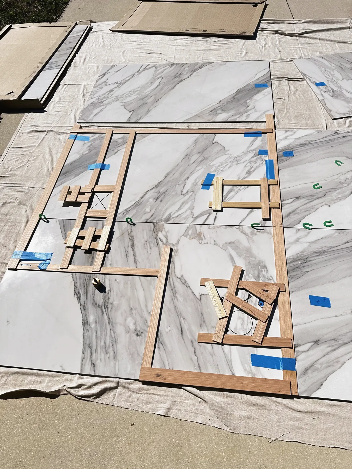 Large marble-look slab laid flat with wooden templates and blue tape marking cut lines