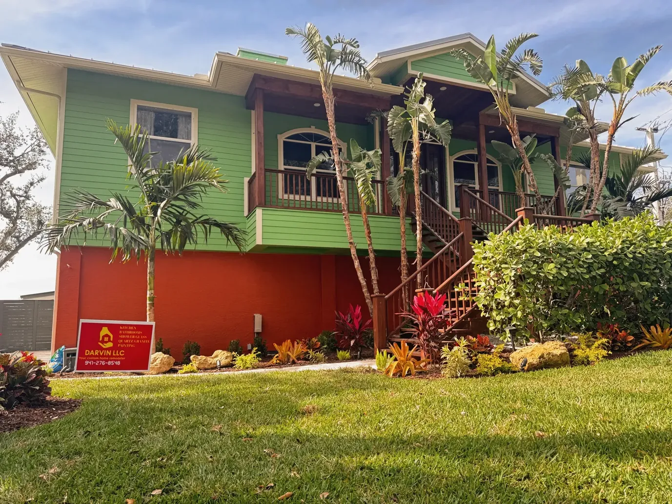 Green two-story house with palm trees, tropical plants and a bright lawn