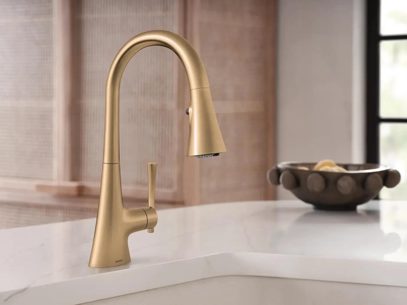 Brushed gold Moen Kurv pull-down faucet on a white stone counter